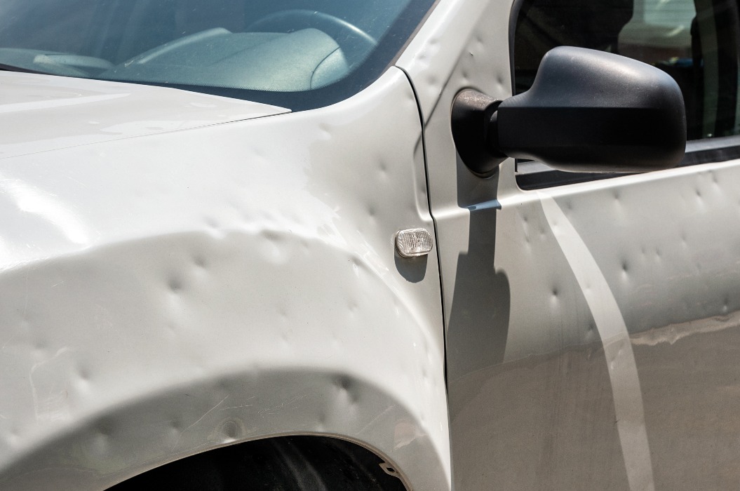 Verbeultes weißes Auto nach Hagelsturm auf der Straße geparkt